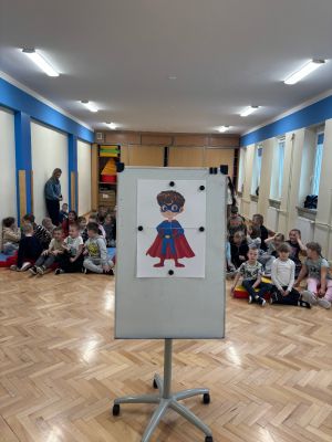 Na środku sali znajduje się plansza z wizerunkiem superbohatera, kt&oacute;ry towarzyszył dzieciom podczas warsztat&oacute;w i pomagał im poznawać &bdquo;supermoce&rdquo; dobrej komunikacji.
