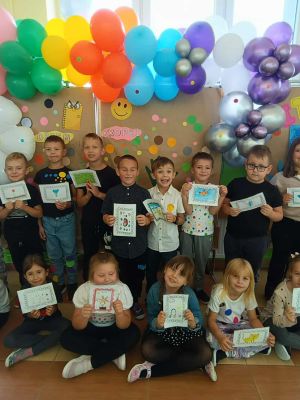 Uczniowie klasy 1a z uśmiechem prezentują swoje kolorowe i pomysłowe prace plastyczne.