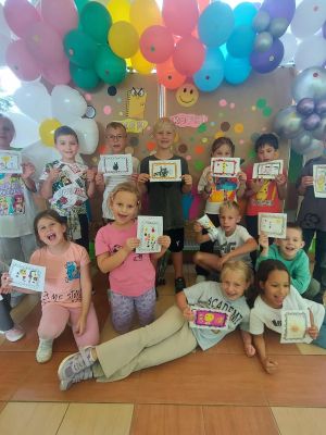 Uczniowie klasy 2b z radością i uśmiechem prezentują swoje kolorowe dzieła plastyczne.