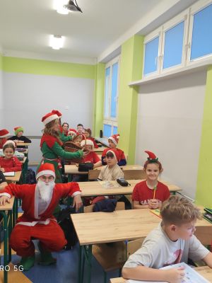 Uczniowie w świątecznych przebraniach rozdają mikołajkowe prezenty.