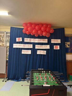 Na tle granatowej kurtyny wisi dekoracja z czerwonych balon&oacute;w i plakat&oacute;w tworzących napis o Międzynarodowym Dniu Przeciwdziałania Przemocy wobec Dzieci.